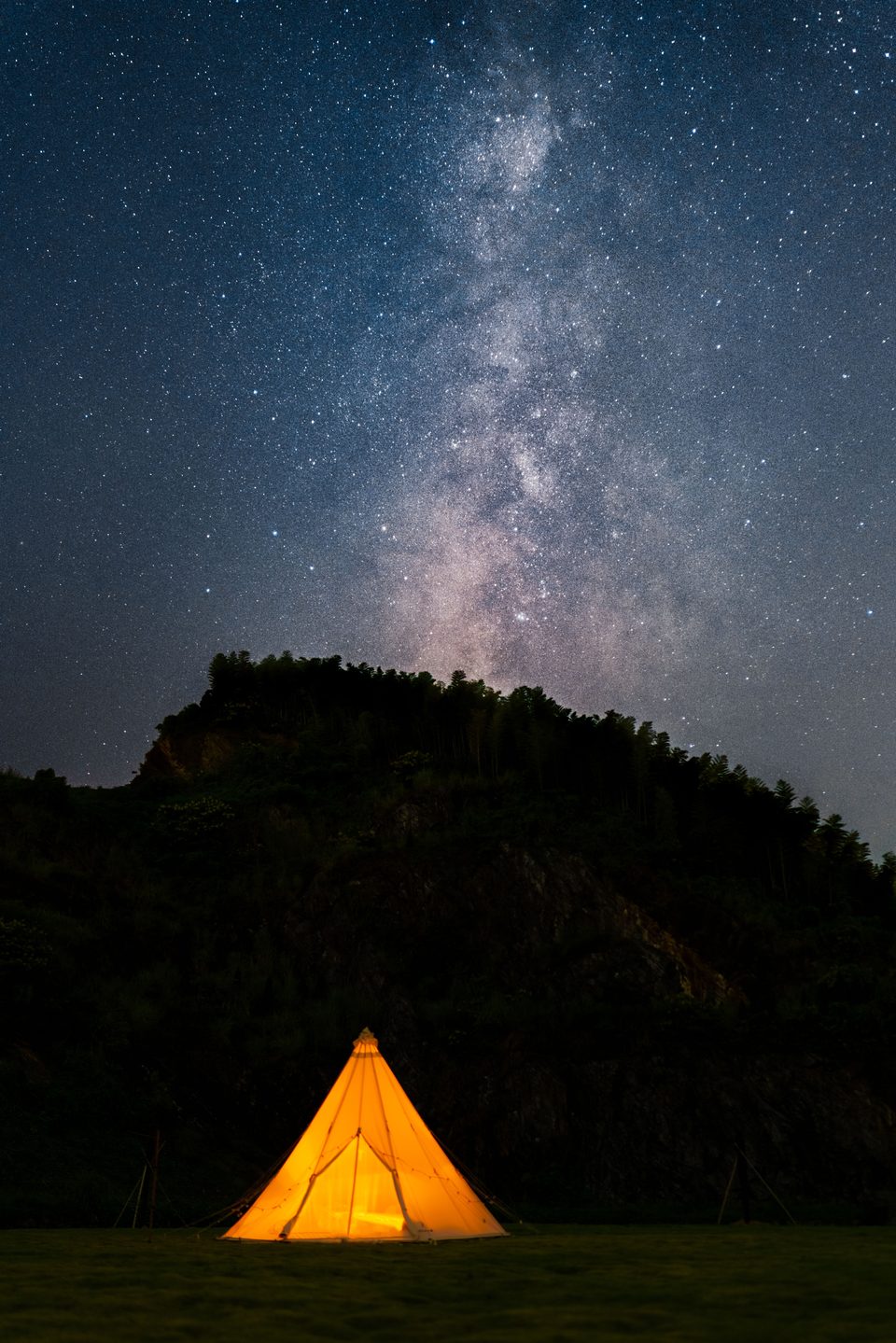 A glowing tent on grass beneath a sky filled with stars